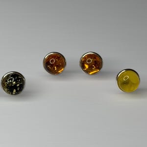 May include: Three pairs of earrings with round amber stones set in silver. The stones are in shades of yellow, orange, and green.