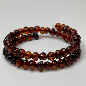 Peut inclure: Un bracelet en ambre brun composé de plusieurs rangs de perles. Le bracelet est enroulé et prêt à être porté.