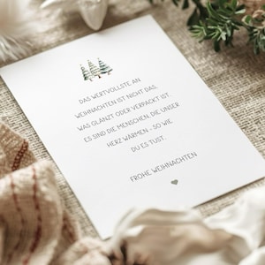 Könnte beinhalten: Eine weiße, rechteckige Grußkarte mit drei kleinen, im Aquarellstil gemalten Weihnachtsbäumen oben und dem Text: DAS WERTVOLLSTE AN WEIHNACHTEN IST NICHT DAS, WAS GLÄNZT ODER VERPACKT IST. ES SIND DIE MENSCHEN, DIE UNSER HERZ WÄRMEN - SO WIE DU ES TUST. FROHE WEIHNACHTEN, ergänzt durch ein kleines Herzsymbol.