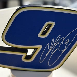 May include: Close-up of a blue number nine with a white and yellow border and a black base. The number has a signature in white. The number is likely a decorative item or part of a larger design.