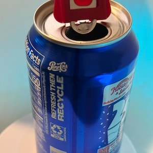 May include: A blue Pepsi can with a red can opener in use. The can has white text that reads "Refresh Then Recycle" and "Holiday World". The can opener is positioned to open the can.