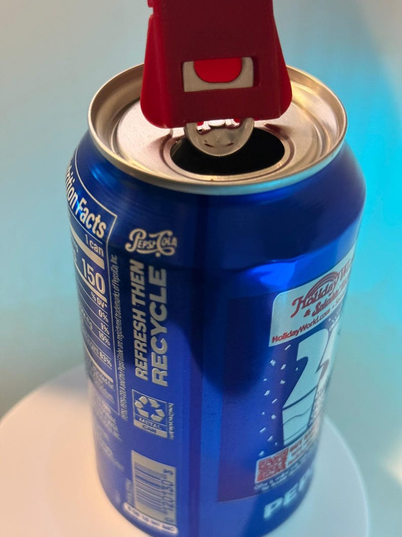 May include: A blue Pepsi can with a red can opener in use. The can has white text that reads "Refresh Then Recycle" and "Holiday World". The can opener is positioned to open the can.