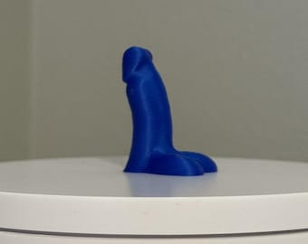 May include: A solid blue, phallic-shaped object. The object is standing upright on a white surface. The object is a vibrant shade of blue and appears to be made of a smooth material.