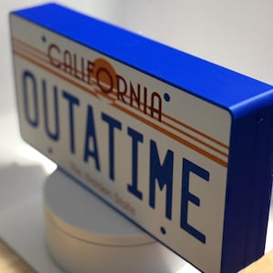 May include: A rectangular sign with a blue border and the words "CALIFORNIA" and "OUTATIME" in blue and orange lettering. The sign also includes the phrase "The Golden State".