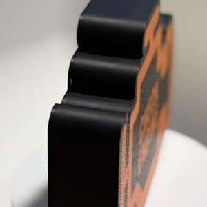May include: A black, three-dimensional object with an orange design. The object has a curved, layered design and is set against a white background. The object appears to be made of a solid material.