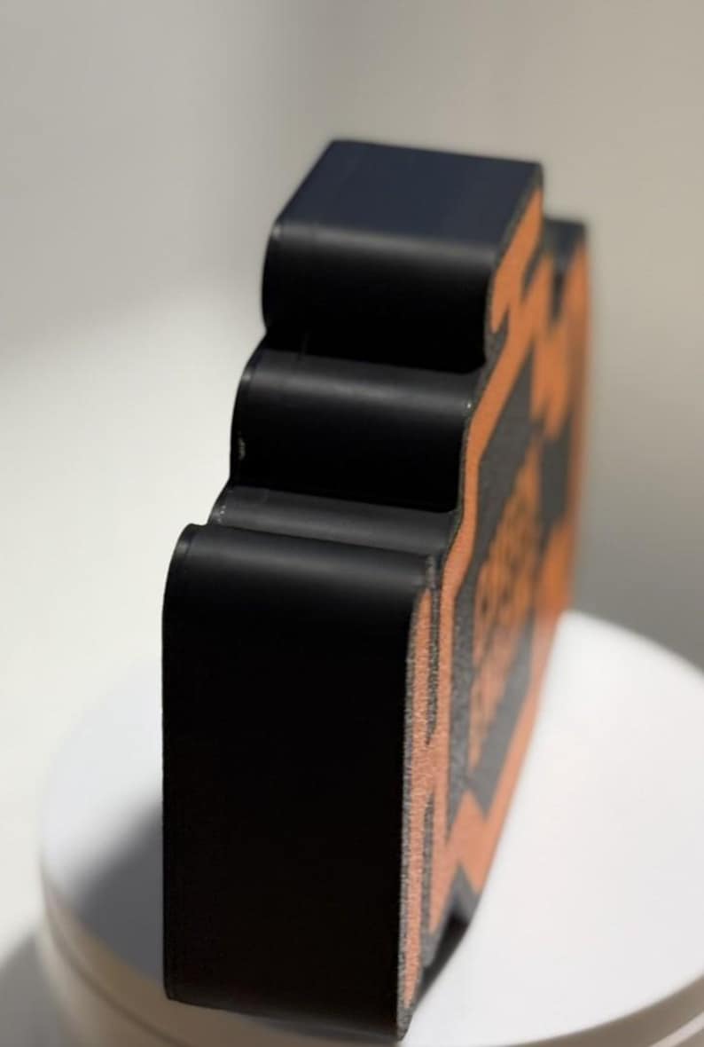 May include: A black, three-dimensional object with an orange design. The object has a curved, layered design and is set against a white background. The object appears to be made of a solid material.