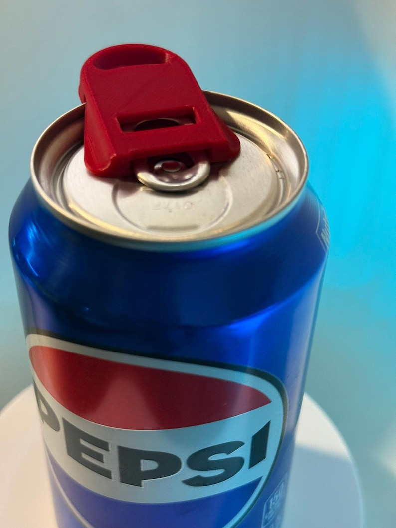 May include: A blue Pepsi can with a red and white logo, topped with a red plastic can opener. The can opener is designed to lift the tab for easy opening. The background is a gradient of blue.