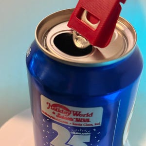 May include: A blue soda can with a red can opener attached to the top. The can has a label that says "Holiday World & Splashin' Safari" and "25 Years". The can opener is designed to easily lift the tab.