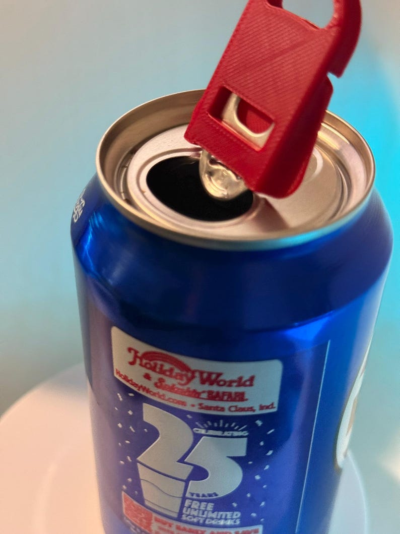 May include: A blue soda can with a red can opener attached to the top. The can has a label that says "Holiday World & Splashin' Safari" and "25 Years". The can opener is designed to easily lift the tab.