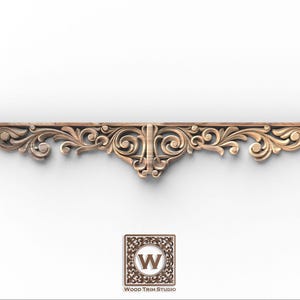 May include: A carved wooden decorative trim piece with an ornate floral and scroll design. The trim is light brown and features symmetrical patterns. The Wood Trim Studio logo is at the bottom.
