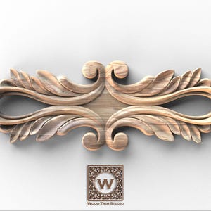 May include: A carved wooden decorative element with a symmetrical design featuring stylized leaves and scrolls. The wood has a natural grain and a light brown color. The logo of Wood Trim Studio is at the bottom.
