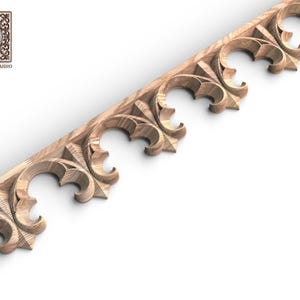 May include: A light brown wooden trim piece featuring a repeating carved pattern of arched, clover-like shapes with pointed tips. The wood grain is visible throughout the piece, which is displayed diagonally. A logo with the text Wood Trim Studio is present.