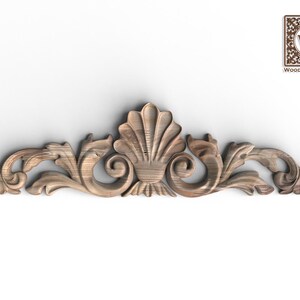May include: A horizontal wooden decorative trim piece featuring a central carved shell motif flanked by symmetrical scrolling acanthus leaf patterns. The wood has a natural brown grain finish. The logo Wood Trim Studio is in the top right corner.
