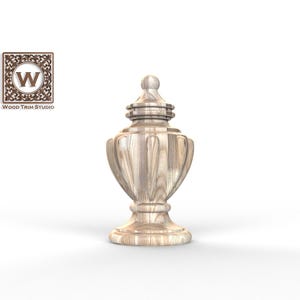 May include: A light-coloured wooden finial with a rounded top, a tiered neck, and a bulbous body featuring vertical fluted carvings. The base is circular and stepped. A square logo in the upper left corner displays the text Wood Trim Studio.