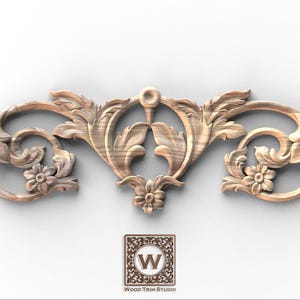 May include: A carved wooden decorative element with a symmetrical design. The piece features floral and scrollwork motifs, including flowers and stylized leaves. The wood has a natural, light brown colour. The logo "Wood Trim Studio" is visible.