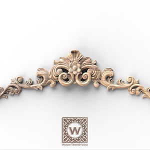 May include: A carved wooden architectural ornament with a floral and scroll design. The light brown piece has a central flower and symmetrical, curved elements. The Wood Trim Studio logo is at the bottom.