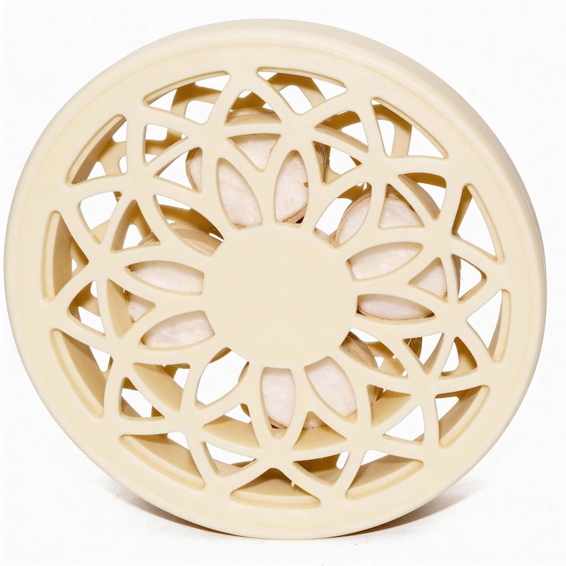 May include: A cream-coloured, circular decorative object with a geometric openwork design. The centre features a solid circle, and the openwork reveals a glimpse of the interior. The object appears to be made of a solid material.