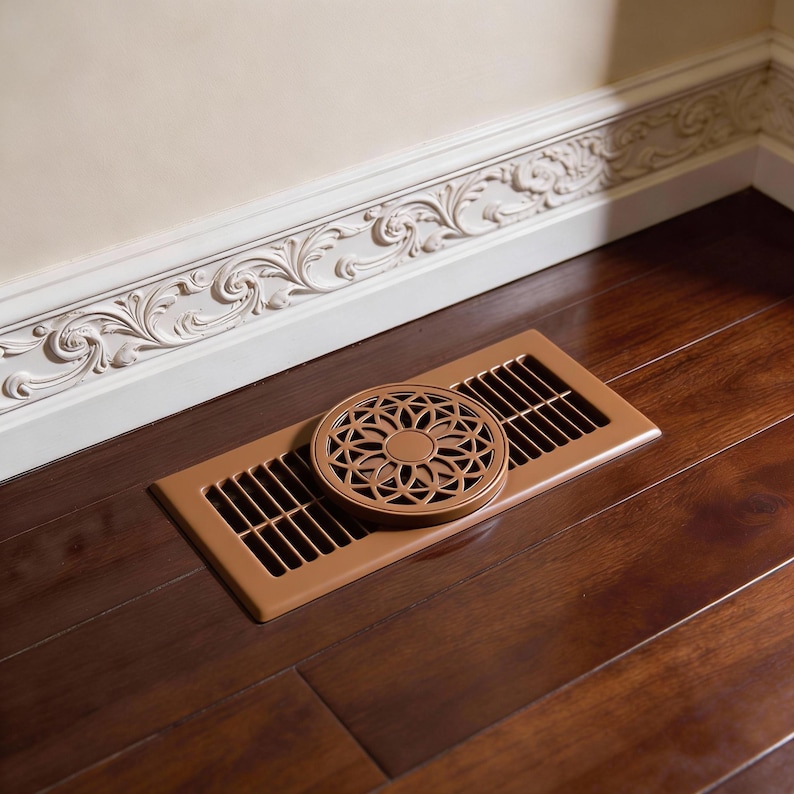 May include: A bronze floor vent with a decorative circular cover featuring a floral design. The vent is rectangular with parallel slots. The cover is placed on top of the vent. The vent is on a dark wood floor.