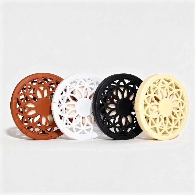 May include: Four round coasters with a floral cutout pattern, arranged side by side. The coasters are in brown, white, black, and cream. They are made of a hard material and are designed to protect surfaces from heat and moisture.