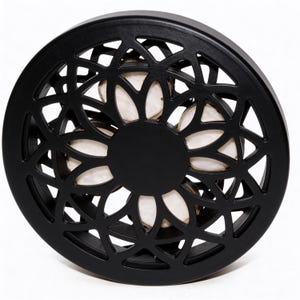 May include: A black, circular decorative object with a floral, openwork design. The centre is solid black, and the openwork reveals a light-coloured interior. The object is likely made of wood or a similar material.