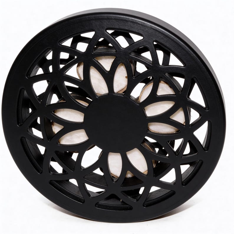May include: A black, circular decorative object with a floral, openwork design. The centre is solid black, and the openwork reveals a light-coloured interior. The object is likely made of wood or a similar material.