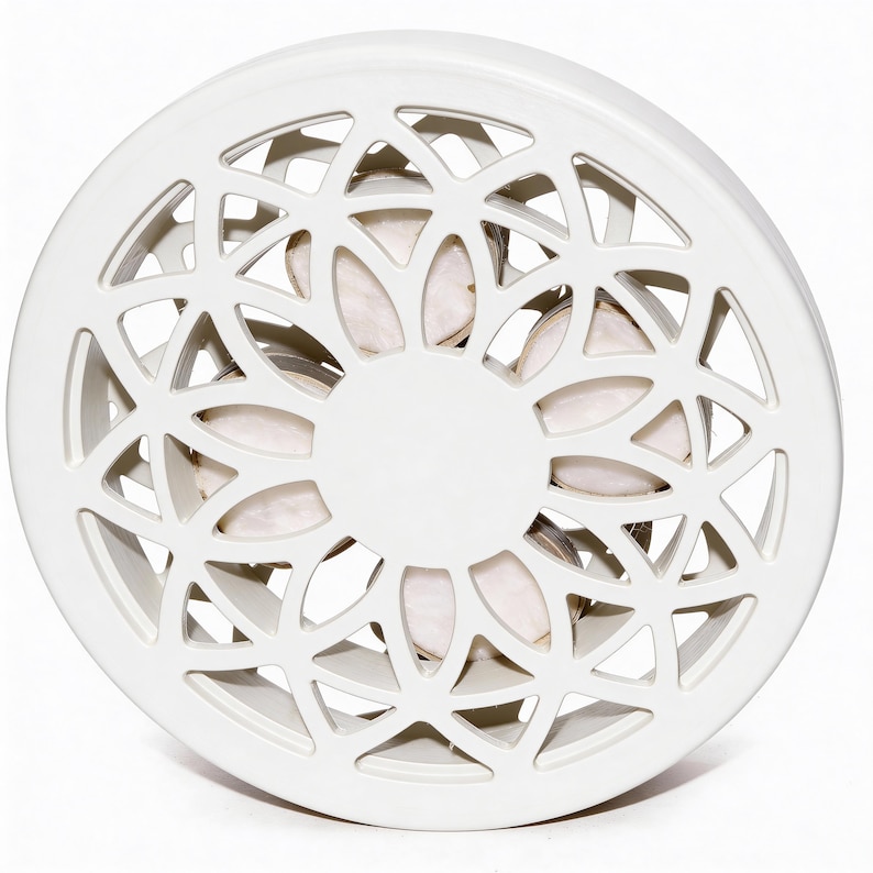 May include: A white, circular decorative object with a geometric, openwork design. The centre features a solid white circle, and the openwork reveals a glimpse of a light-coloured interior. The object is likely made of ceramic or a similar material.
