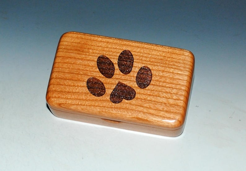 Small handmade in the USA natural cherry wood box with an engraved paw print with a heart about the size of a business card. Sanded to perfection and finished with many coats of tung oil. Interior is fully lined with blown in rayon fibers.