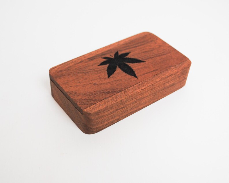 May include: A small wooden box with a dark brown finish. The top of the box has a black leaf design.