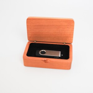 May include: A wooden box with a hinged lid, open to reveal a silver and black USB flash drive inside.