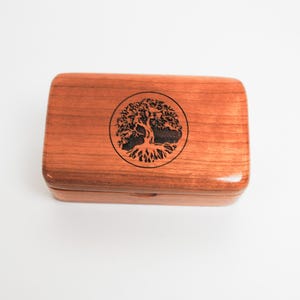May include: A small wooden box with a hinged lid. The box is made of cherry wood and has a tree of life design engraved on the top.