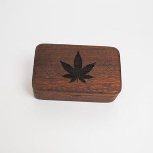 May include: A small wooden box with a dark brown finish. The box has a black leaf design on the top.