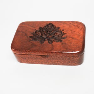 May include: A small wooden box with a dark red finish. The top of the box features a laser-etched design of a mandala with intricate details.