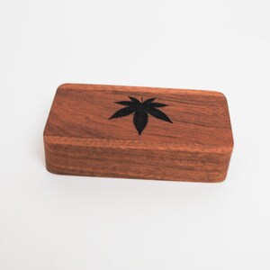 May include: A wooden box with a black leaf design. The box is made of dark wood and has a smooth finish.