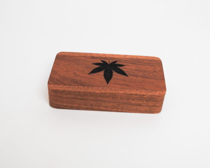 May include: A wooden box with a black leaf design. The box is made of dark wood and has a smooth finish.
