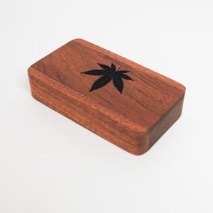May include: A small wooden box with a dark brown finish. The box has a black leaf design on the top.