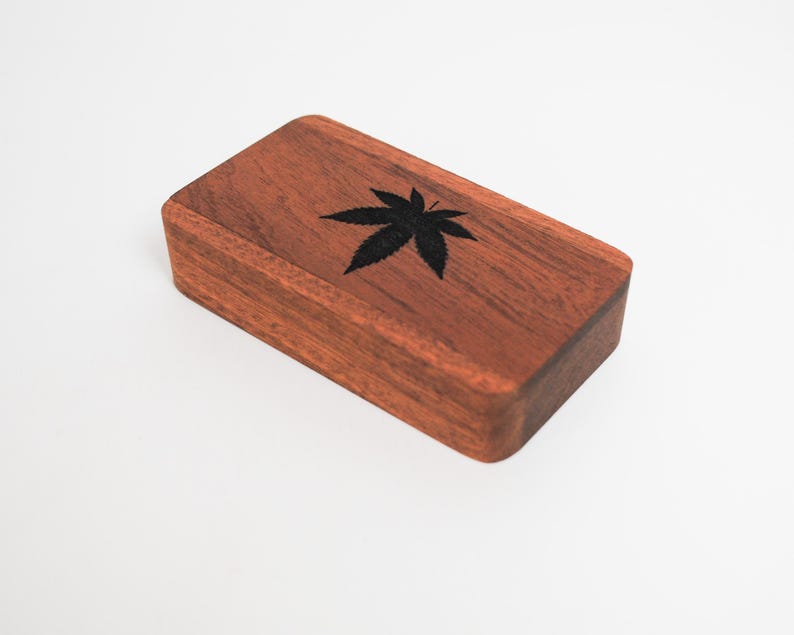 May include: A small wooden box with a dark brown finish. The box has a black leaf design on the top.