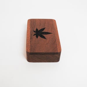 May include: A small wooden box with a dark brown finish. The box has a black leaf design on the top.
