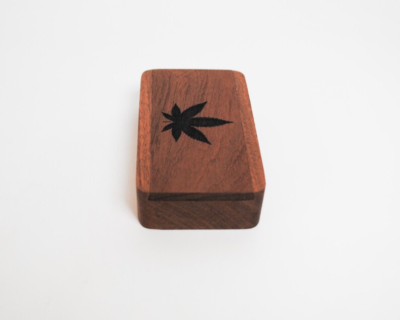 May include: A small wooden box with a dark brown finish. The box has a black leaf design on the top.