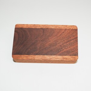 May include: A rectangular wooden box with a dark brown walnut wood top and a lighter brown wood border.