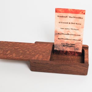 May include: A wooden box with a hinged lid, open to reveal a business card inside. The business card is for Woodstuff/Burl WoodBox, with contact information for Al Freund & Deb Keese, including their website and Etsy shop name.