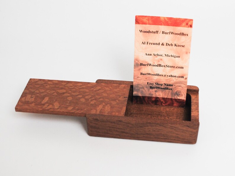 May include: A wooden box with a hinged lid, open to reveal a business card inside. The business card is for Woodstuff/Burl WoodBox, with contact information for Al Freund & Deb Keese, including their website and Etsy shop name.