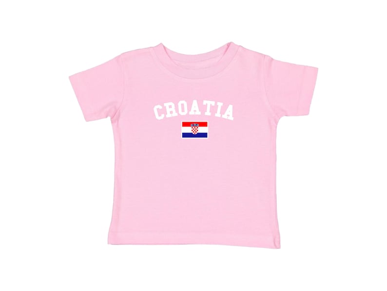 May include: A light pink t-shirt with the word "CROATIA" in white arched letters above the Croatian flag. The flag is a red, white, and blue checkered design with a coat of arms.