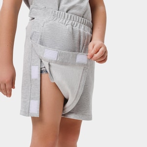 May include: Light gray adaptive shorts with a wrap-around design. The shorts feature a soft, elastic waistband and are secured with white hook-and-loop fasteners. The shorts are made of a comfortable, breathable fabric.