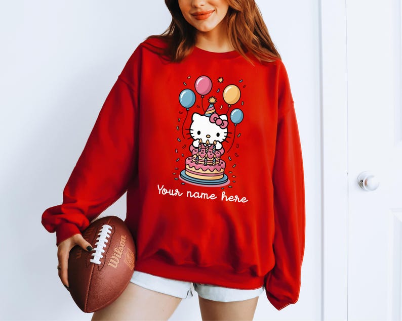 May include: Red sweatshirt featuring a cartoon character with a birthday cake and balloons. The graphic includes the text "Your name here". The sweatshirt is a long-sleeved, casual top.