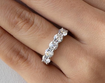 May include: A close-up of a ring with multiple round, clear gemstones set in a silver band. The ring is on a hand with light pink nail polish. The background is a white fabric.