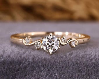 Könnte beinhalten: Ein goldener Ring mit einem großen, runden, klaren Edelstein in der Mitte. Der Ring hat ein zartes, wirbelndes Design mit kleineren Akzentsteinen. Der Ring ist vor einem grauen Hintergrund platziert, der das Funkeln der Edelsteine hervorhebt.
