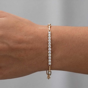 May include: A gold bracelet featuring a line of small, clear gemstones. The bracelet is fastened with a clasp. The bracelet is on a person's arm.