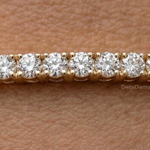 May include: A gold bracelet with nine round diamonds set in individual prongs. The bracelet has a delicate chain design. The diamonds are displayed against a skin tone background. The bracelet is a piece of jewellery.