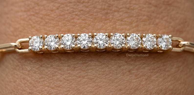 May include: A gold bracelet with nine round diamonds set in individual prongs. The bracelet has a delicate chain design. The diamonds are displayed against a skin tone background. The bracelet is a piece of jewellery.