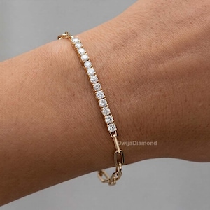 May include: A gold bracelet with a line of clear, round gemstones. The bracelet has a delicate design with a chain-link clasp. The gemstones are set in a gold band, creating a sparkling and elegant accessory.